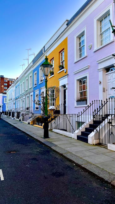 Photograph of a row of Victorian terraced houses in Notting Hill with pastel-colored facades, including shades of white, pale blue, pink, and peach. The buildings feature large sash windows, some with
